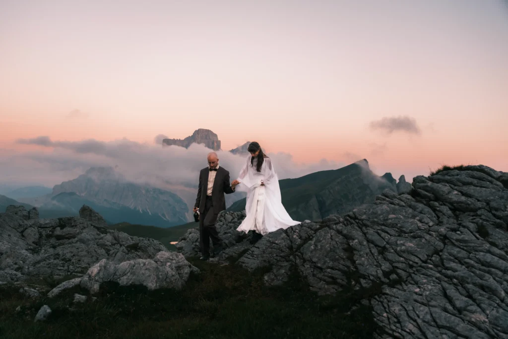 Bride lifting her dress as the couple explore a rocky ridge at dusk.