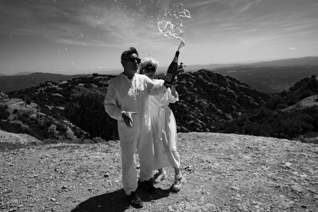 Black-and-white photograph of a couple celebrating with champagne at a mountain viewpoint.