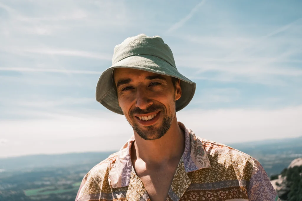 Portrait of Elias smiling in a sun hat outdoors.