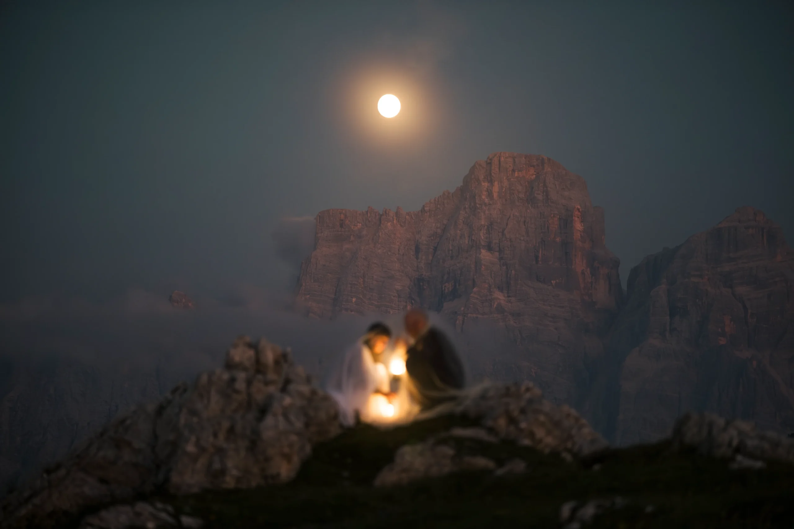Laternenlicht beleuchtet ein Paar unter einem mondbeschienenen Berggipfel.
