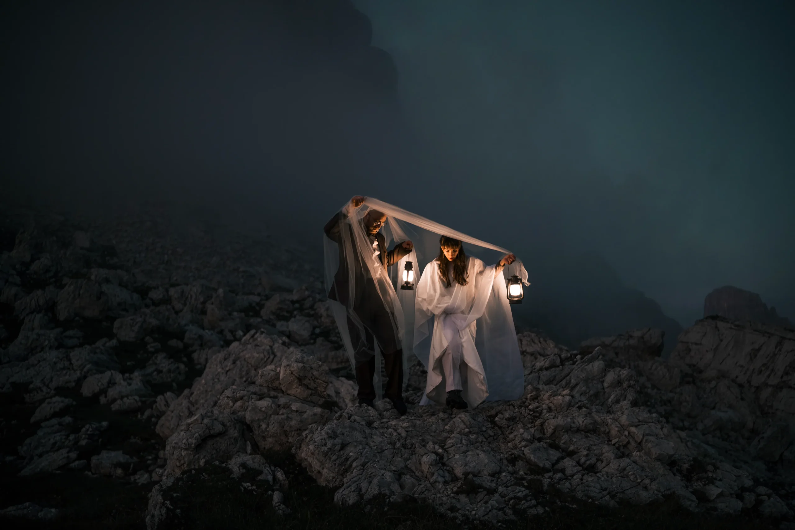 Paar hält in der Dämmerung Laternen unter einem Schleier auf einem Bergweg.