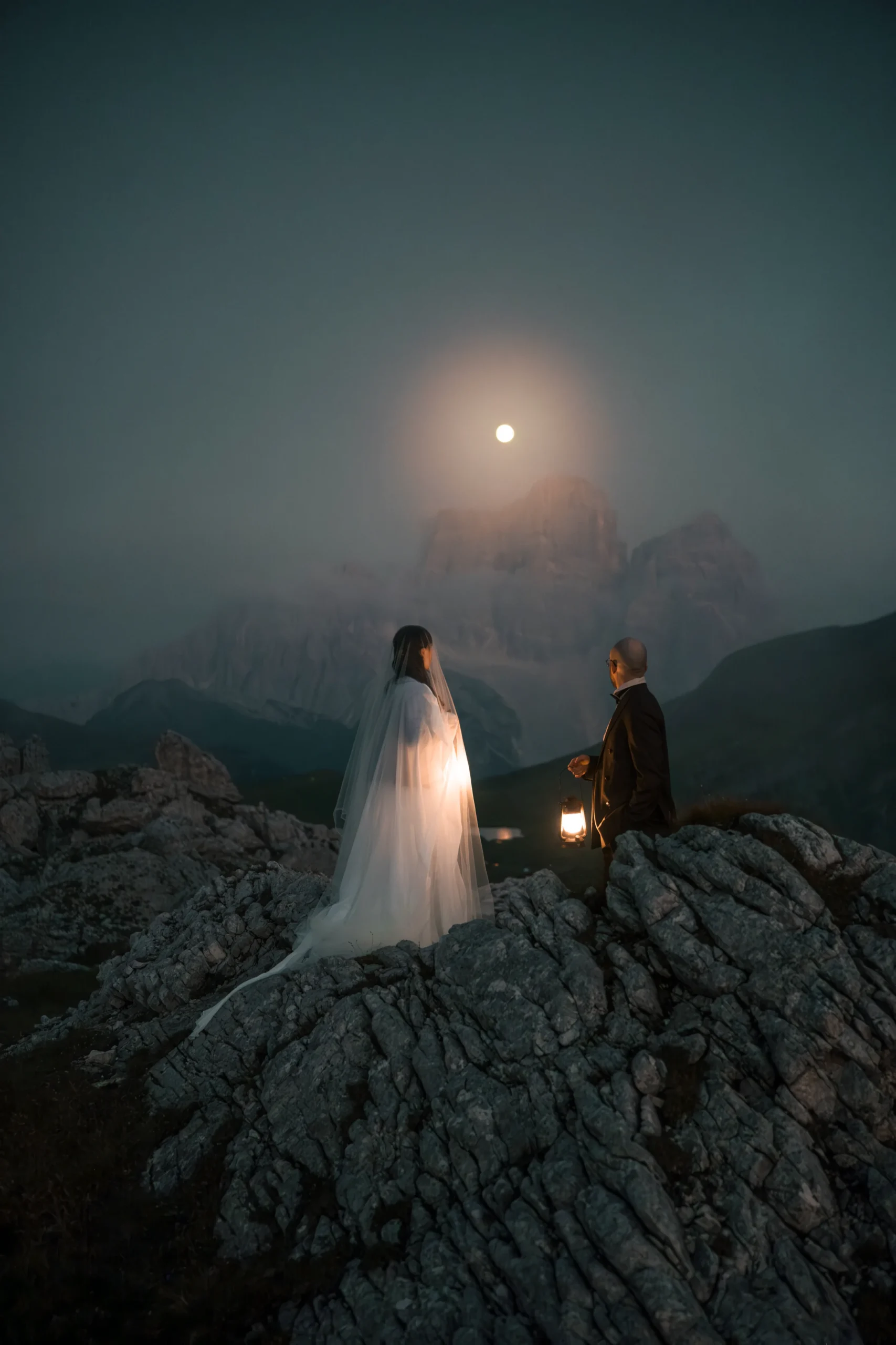 Paar hält Laternen auf einem felsigen Berggrat unter dem Mond.