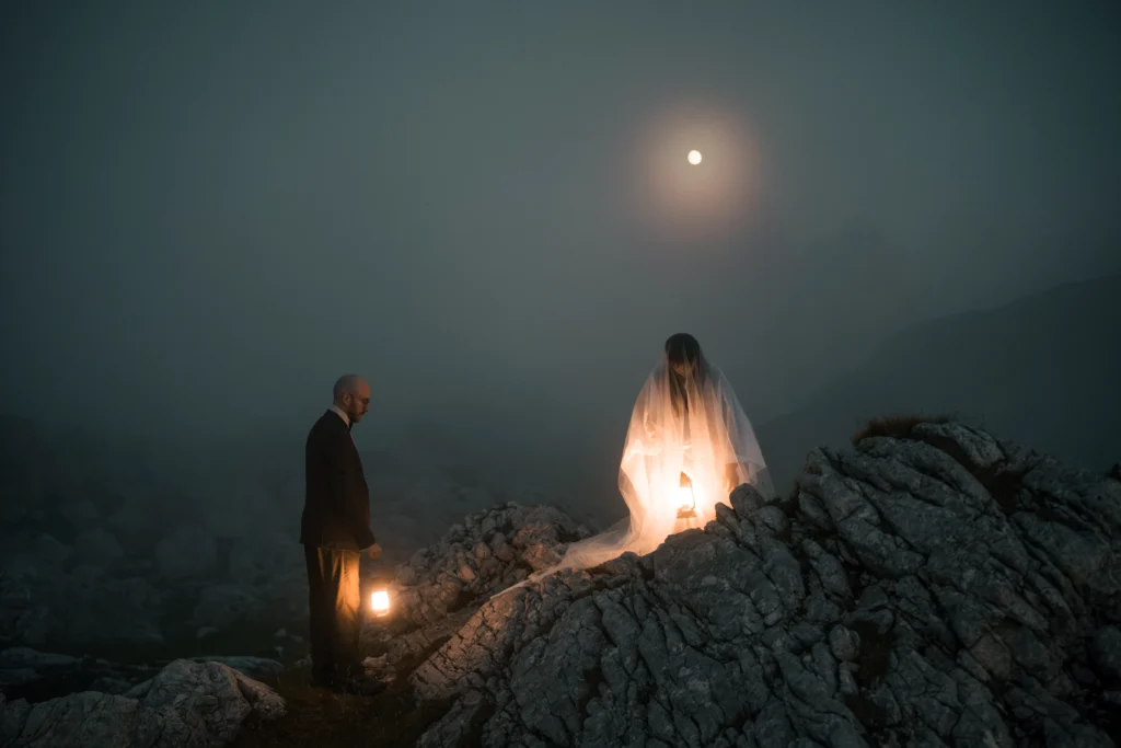 Couple standing among rocks with lanterns under the moon.