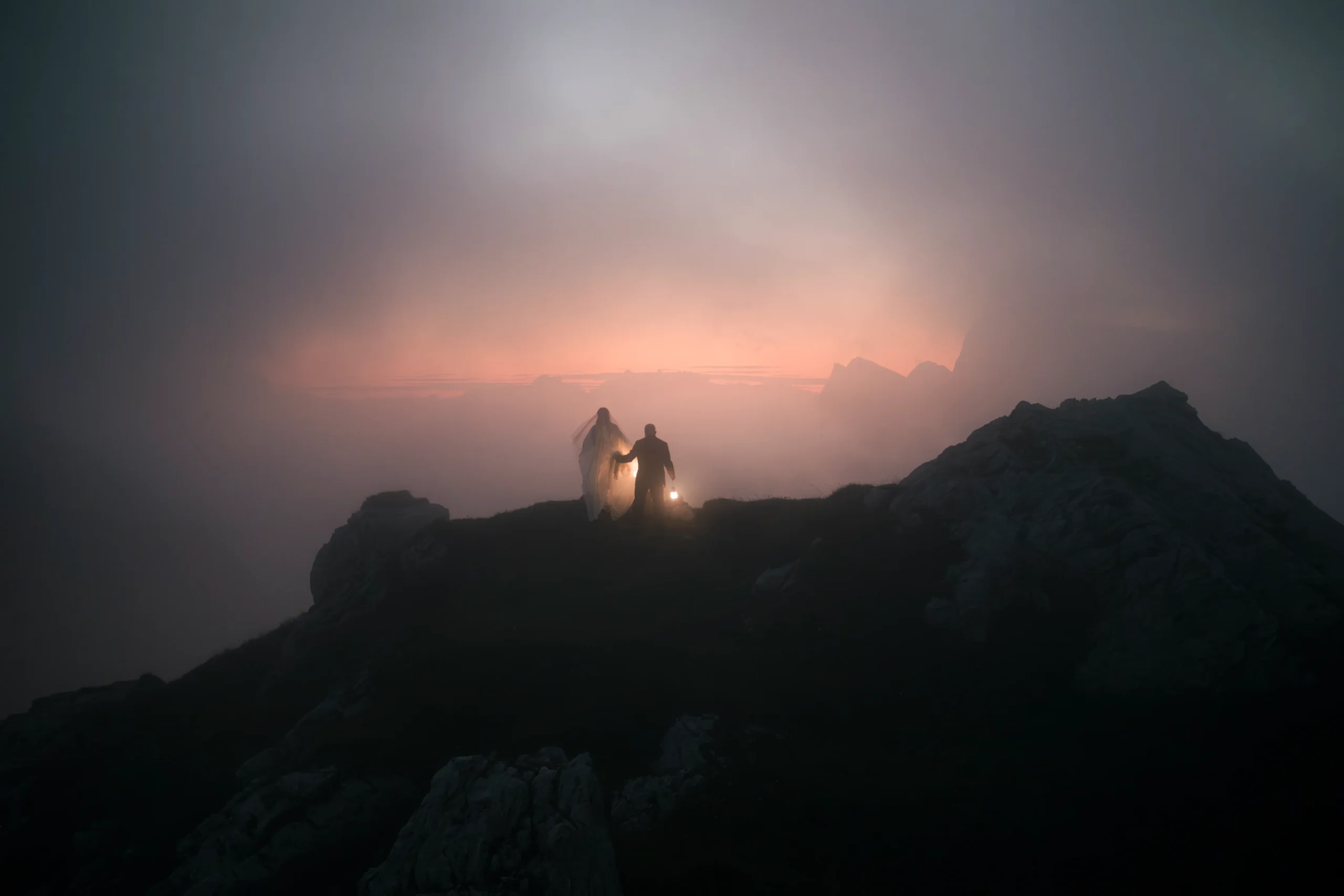 Entferntes Paar mit Laterne als Silhouette vor dem letzten Licht auf einem Berggrat.