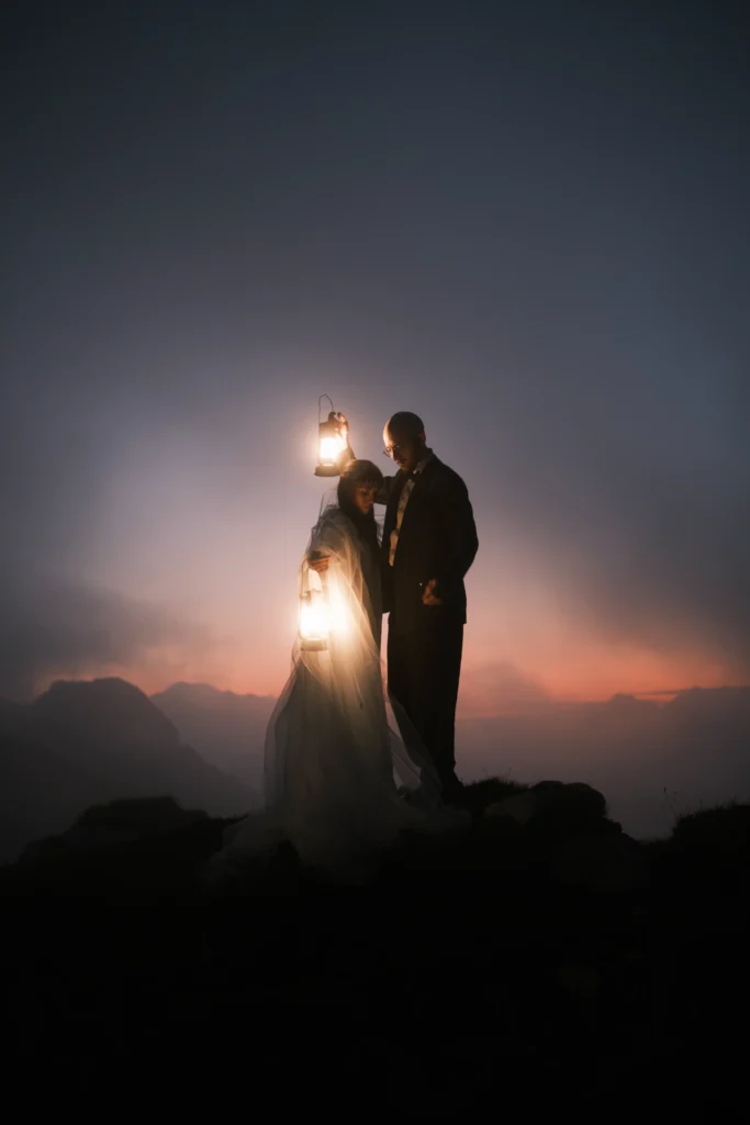 Vertical portrait of a couple with a lantern beneath a darkening mountain sky.