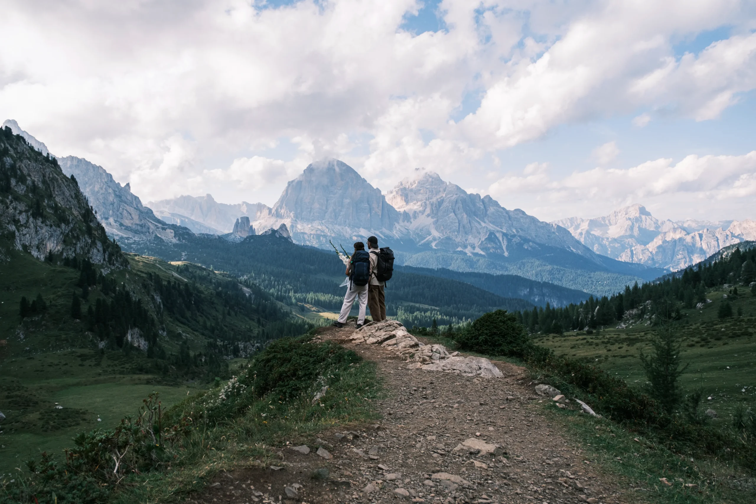 Paar mit Wanderrucksäcken blickt über ein grünes Tal und markante Berggipfel.