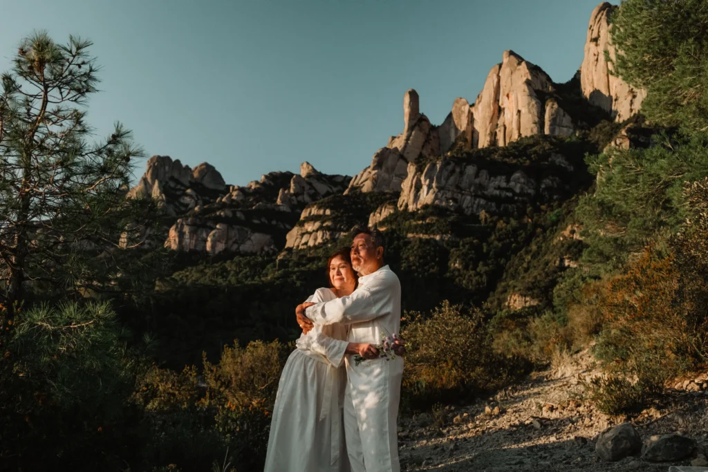 Couple embracing beneath tall, jagged cliffs.